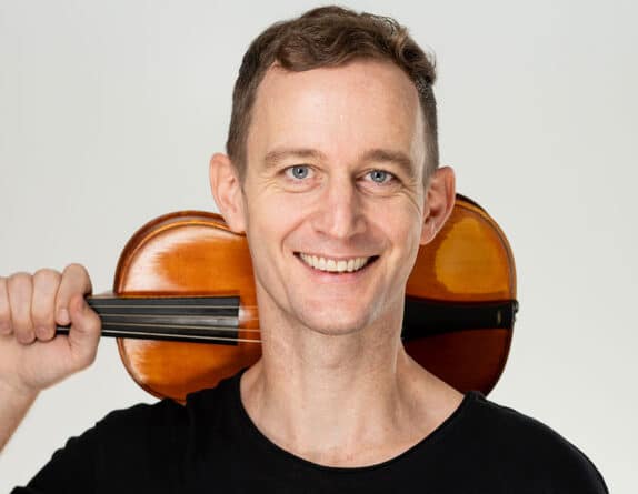 Andrew Fouts holding his violin behind his head