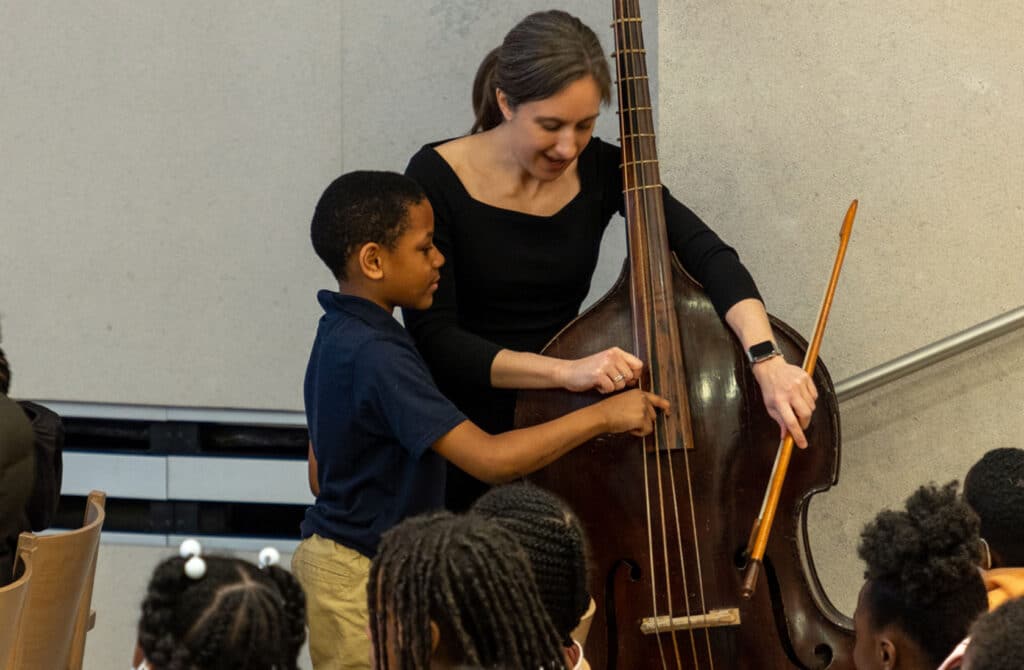 A woman teaching a young black boy about the double bass