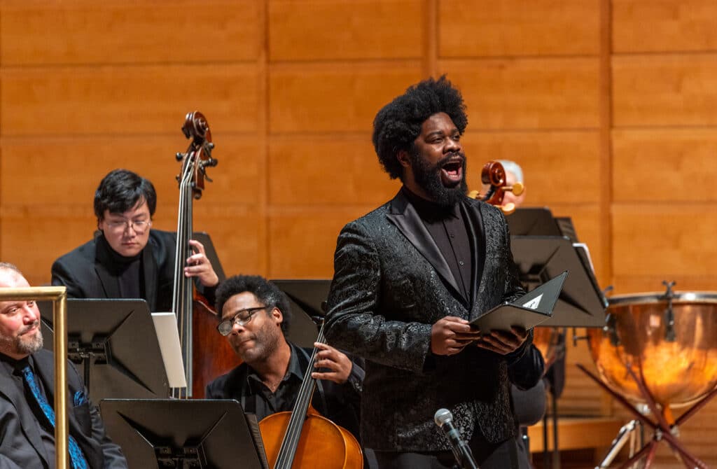 Black male vocalist singing with cellists in the background